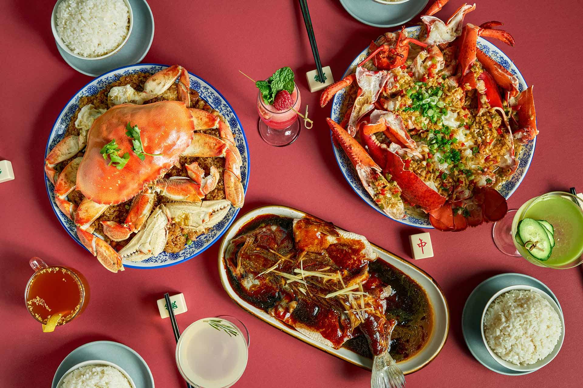 A vibrant spread of Chinese seafood dishes, including whole crab, lobster, and fish in sauce, surrounded by bowls of rice, drinks, and chopsticks on a red table.