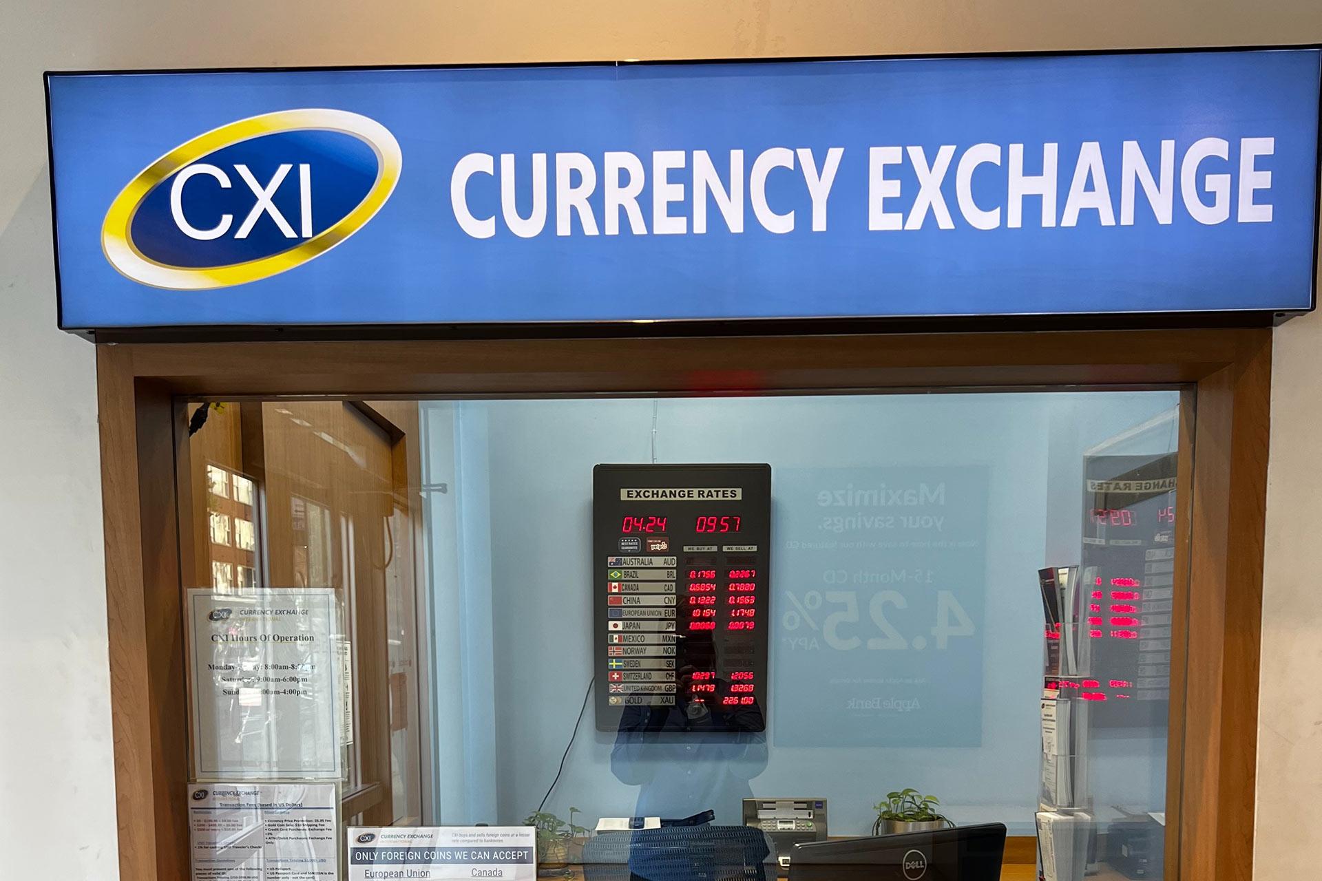 A CXI Currency Exchange booth with a digital display showing exchange rates and a window for customer service, decorated with informational signs and notices.