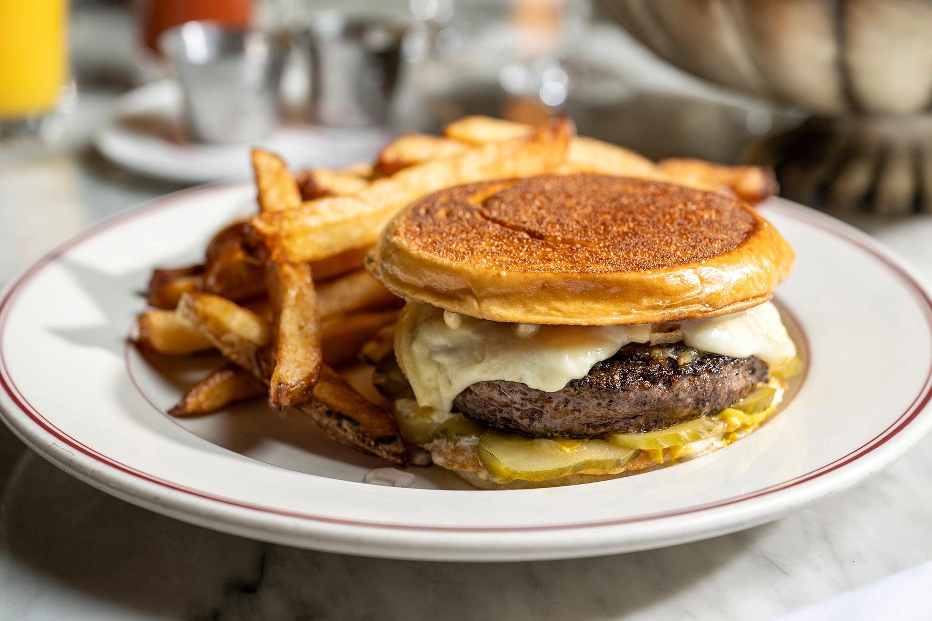 A plate with a cheeseburger featuring melted cheese, pickles, and a toasted bun, served with a side of golden French fries.