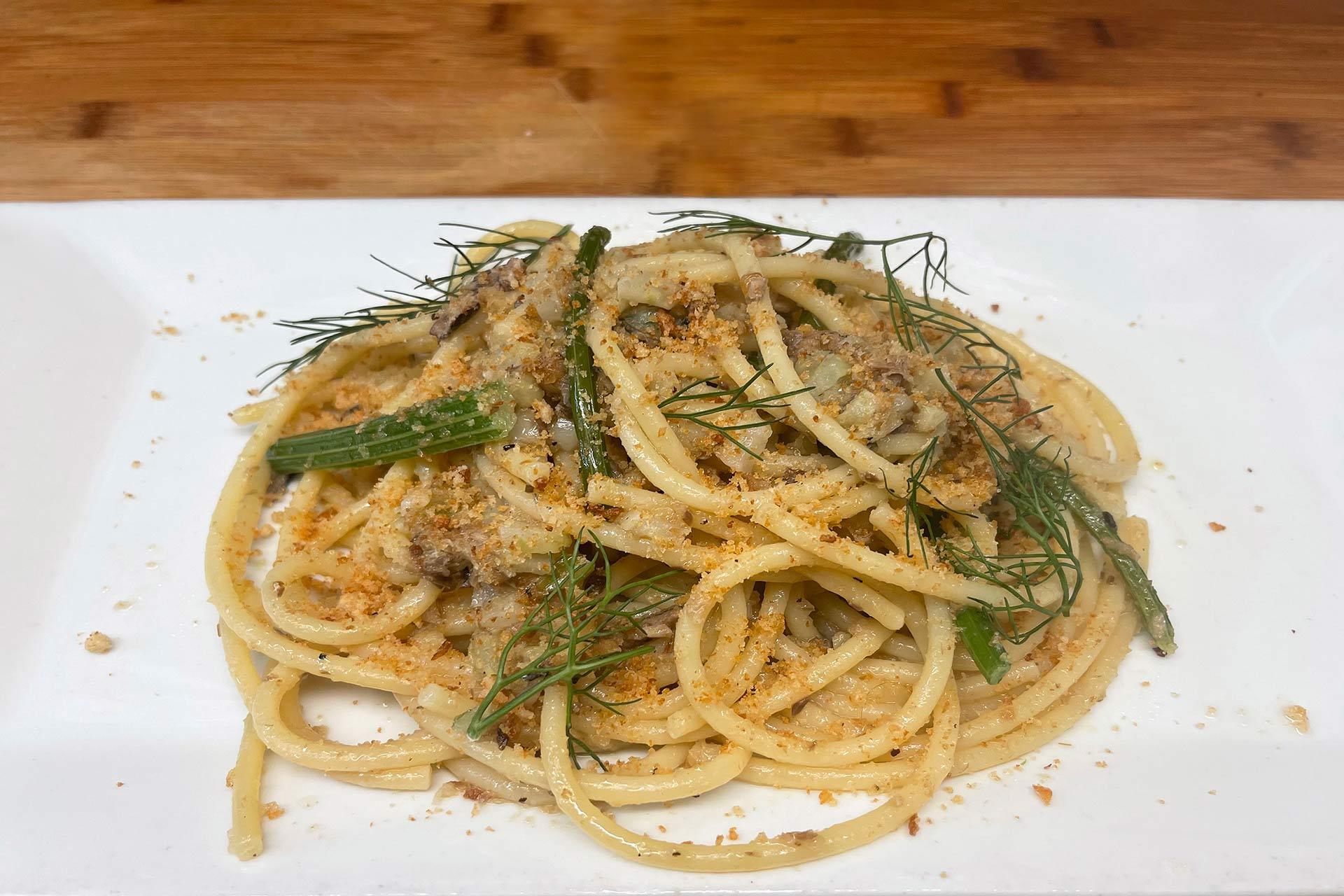 A plate of pasta with sausage, green beans, and herbs, garnished with fresh dill and breadcrumbs, served on a white rectangular dish on a wooden table.