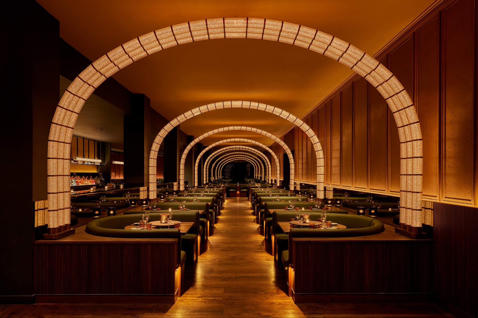 Elegant restaurant interior with warm lighting, featuring multiple illuminated arches over rows of green booth seating and neatly set tables, creating a cozy and inviting dining atmosphere.