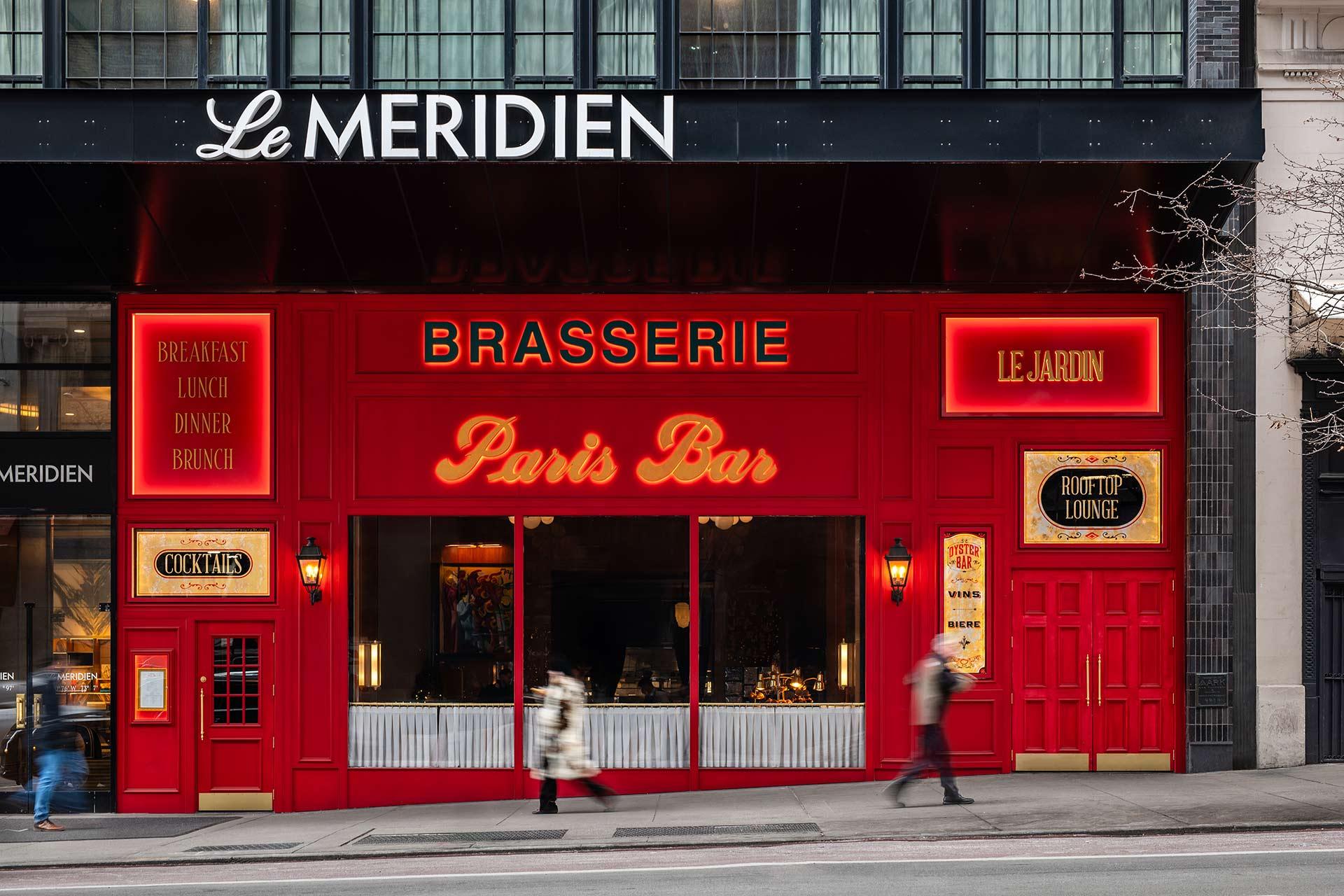A bright red Parisian-style brasserie called "Paris Bar" with neon signs, large windows, and people walking by, located beneath the Le Meridien hotel.