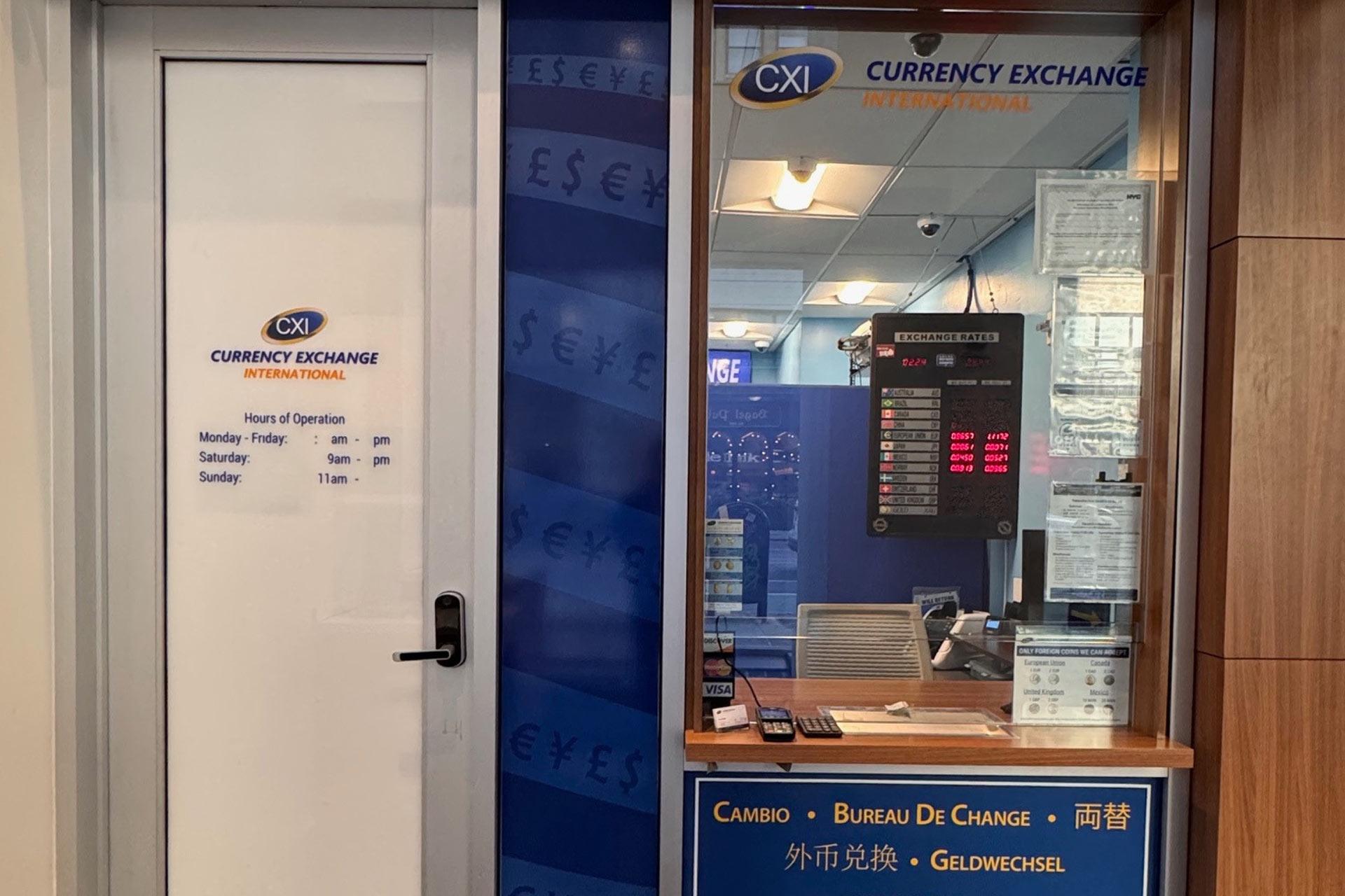 A currency exchange booth with a glass window, illuminated sign, and electronic rate board; hours of operation are posted on a door to the left, listing Monday-Saturday 9am-7pm and Sunday 11am-7pm.