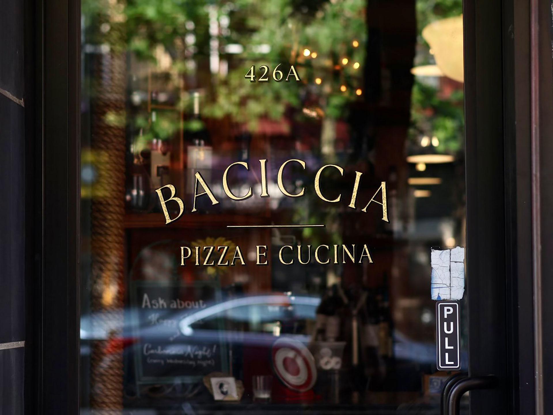 A glass door with gold lettering that reads "BACICCIA PIZZA E CUCINA" and the address "426A." A "PULL" sticker is on the right, and the restaurant interior is faintly visible through the glass.