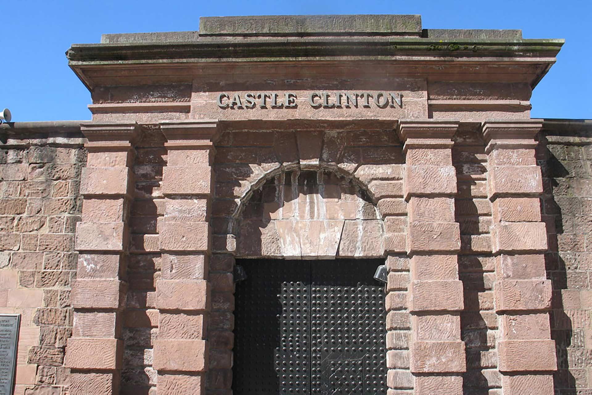 A close-up view of the entrance to Castle Clinton, a historic stone fort with an arched doorway and the name "CASTLE CLINTON" engraved above the entrance.