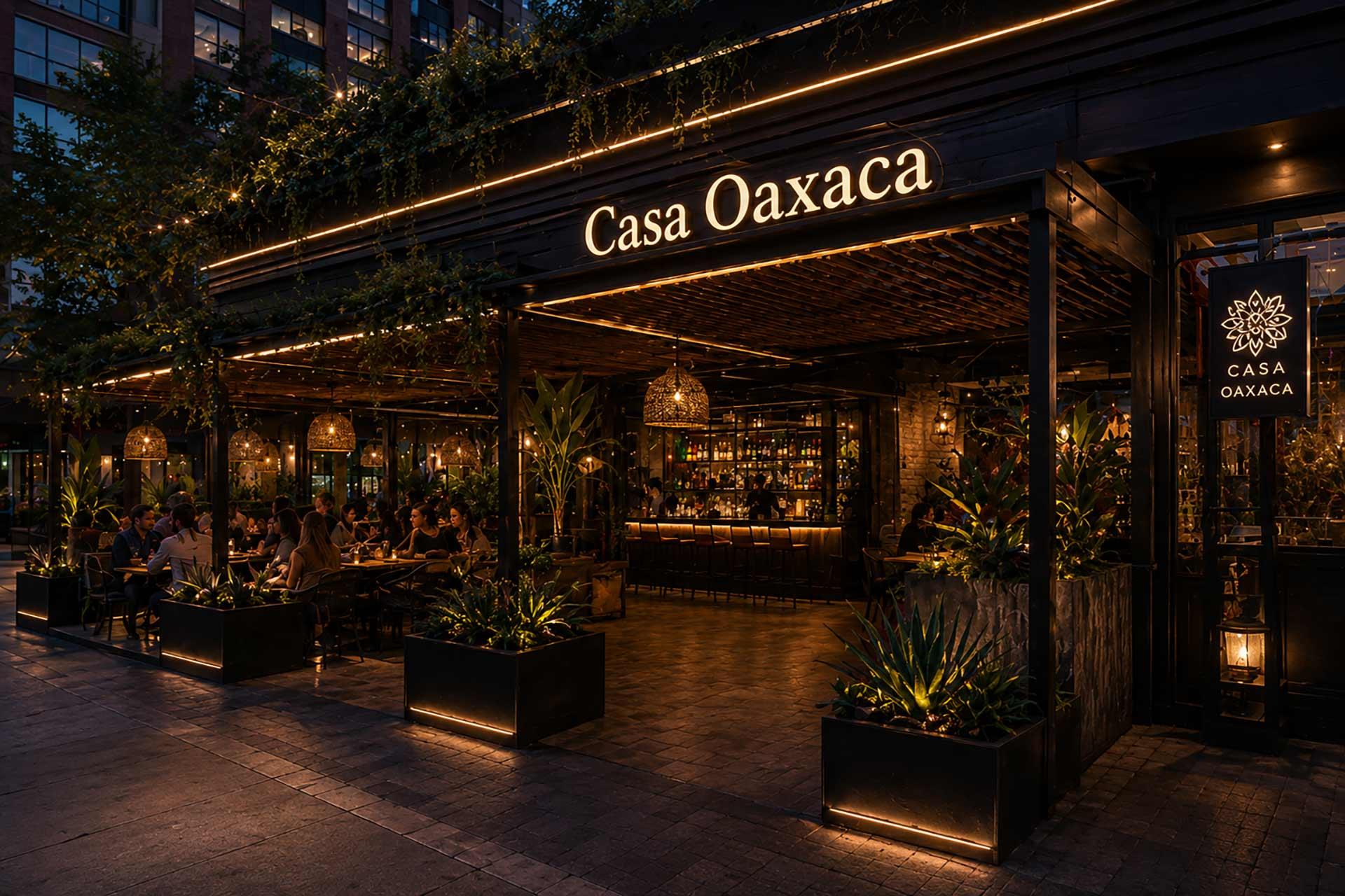 A warmly lit restaurant called Casa Oaxaca with outdoor seating, lush greenery, and people dining in the evening. The entrance and sign are illuminated, creating an inviting and cozy atmosphere.