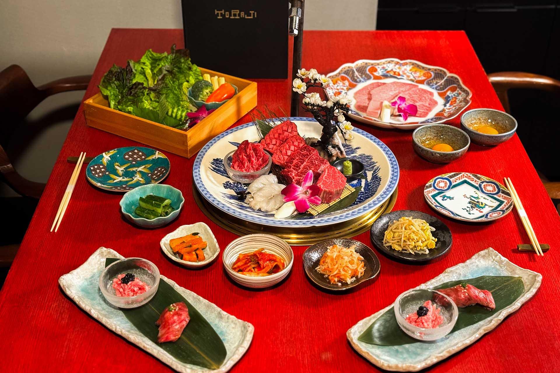 A vibrant Japanese meal on a red table features assorted sushi, sashimi, sauces, vegetables, and garnishes arranged in decorative plates, with orchids used as accents.